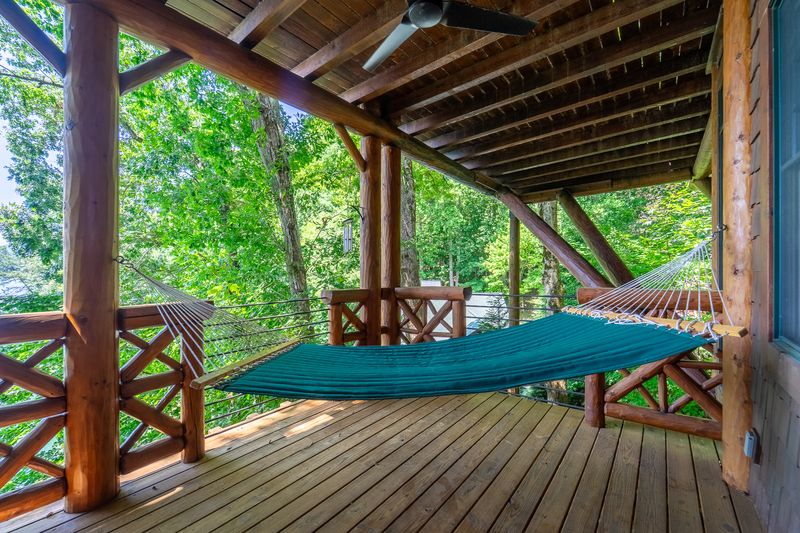 Covered deck with a hammock and log railings above the trees